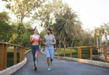 Lächelndes Paar im Gespräch und beim Joggen im Park - CAVF42760