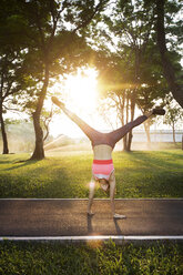 Woman performing handstand on road against trees in sunny day - CAVF42763