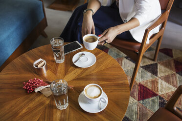 Mittelteil einer Geschäftsfrau mit Kaffeetasse am Tisch in einer Hotellobby - CAVF42773