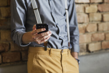 Midsection of businessman using smart phone against brick wall in hotel - CAVF42776