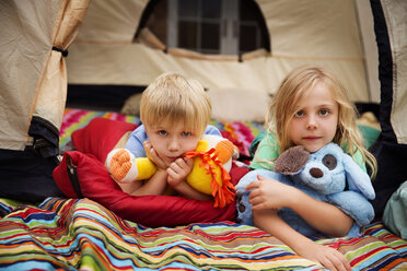 Portrait von Geschwistern mit Plüschtieren im Zelt liegend - CAVF42820