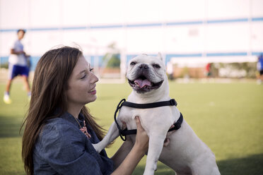 Happy woman playing with dog on grassy field at park - CAVF42858