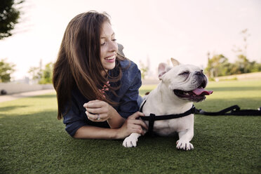 Happy woman lying with dog on grassy field at park - CAVF42859