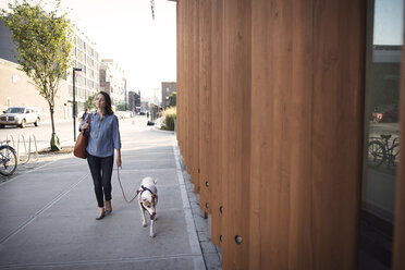 Nachdenkliche Frau mit Hund auf dem Gehweg an einer Holzwand in der Stadt - CAVF42865