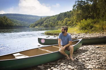 Mann schaut weg, während er auf einem Kanu am Seeufer sitzt - CAVF42890