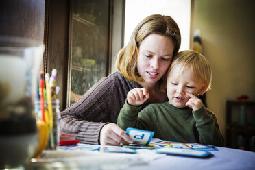 Mother showing cards to son while sitting at table - CAVF42956