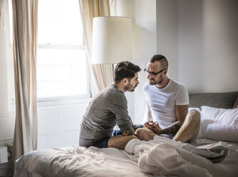 Gay men holding hands while sitting on bed at home - CAVF43006