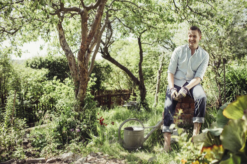 Glücklicher junger Mann entspannt sich bei der Gartenarbeit im Garten - MASF04931