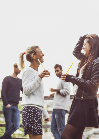 Glückliche Freundinnen mit Holunderblütengetränken auf einer Dachterrassenparty, lizenzfreies Stockfoto