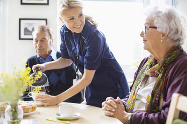 Happy female caretaker serving coffee to senior people at nursing home - MASF04943