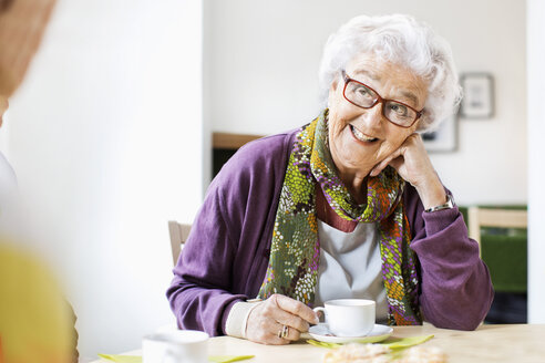 Glückliche ältere Frau sieht ihren Freund an, während sie am Frühstückstisch im Pflegeheim Kaffee trinkt - MASF04944