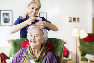 Glückliche Pflegerin, die einer älteren Frau im Pflegeheim Lockenwickler aufs Haar legt - MASF04947