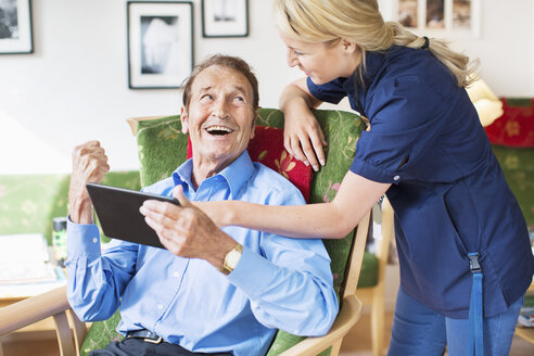 Glücklicher älterer Mann und weibliche Betreuerin verwenden digitales Tablet im Pflegeheim - MASF04949