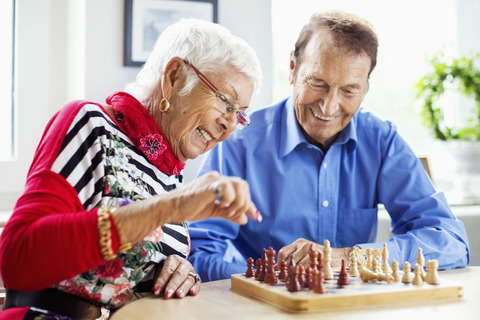 Glückliches Seniorenpaar spielt Schach am Tisch im Pflegeheim, lizenzfreies Stockfoto