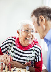 Happy senior couple looking at each other while playing chess in nursing home - MASF04955