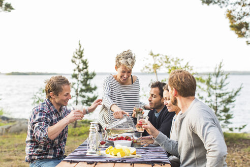 Glückliche Frau serviert Freunden beim Mittagessen am Seeufer Bier - MASF04963