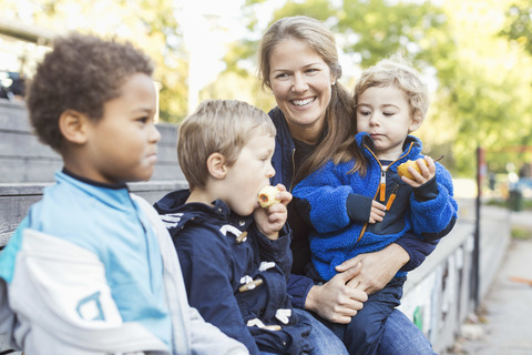 Glückliche Lehrerin sitzt mit Kindern vor dem Kindergarten, lizenzfreies Stockfoto