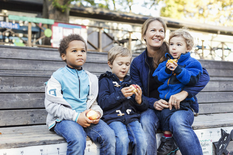 Glückliche Lehrerin sitzt mit Kindern vor dem Kindergarten, lizenzfreies Stockfoto