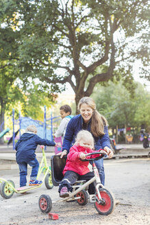 Happy teacher assisting girl to ride tricycle on playground - MASF04984