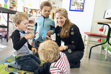Glückliche Lehrerin und Kinder spielen mit Seifenblasen im Kindergarten - MASF04986