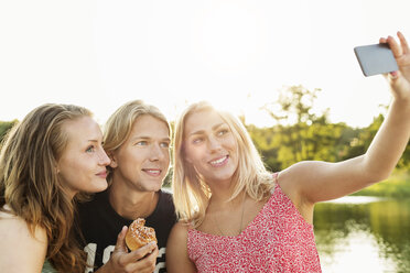 Glückliche Freunde machen ein Selfie beim Frühstück am See gegen den klaren Himmel - MASF04989