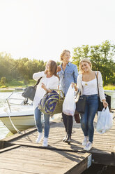 Happy friends with luggage walking on pier by lake against clear sky - MASF04991