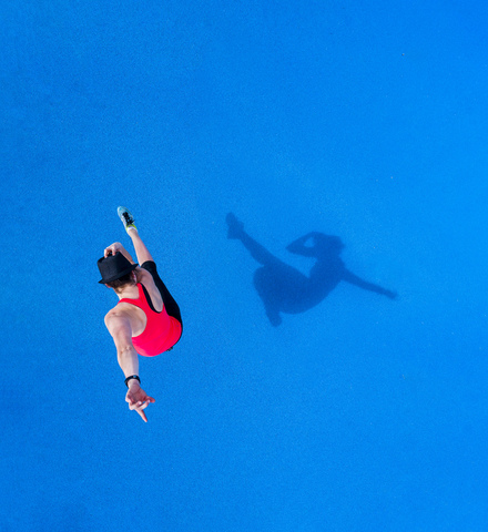 Springende junge Frau und ihr Schatten auf blauem Hintergrund, Ansicht von oben, lizenzfreies Stockfoto