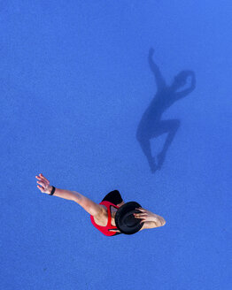 Springende junge Frau und ihr Schatten auf blauem Hintergrund, Ansicht von oben - STSF01492