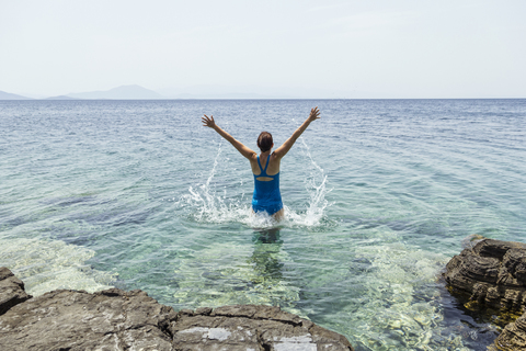 Greece, Lefokastro, woman jumping into water, raised arms stock photo