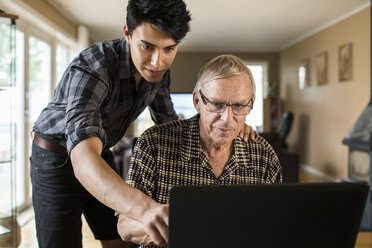 Grandson assisting grandfather in using laptop at home - MASF05006