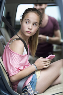 Mädchen mit Mobiltelefon, das wegschaut, während es im Auto sitzt, mit Vater im Hintergrund - MASF05009