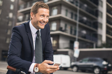 Happy businessman using smart phone in city - MASF05019