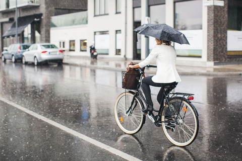 Volle Länge Rückansicht der Geschäftsfrau Reiten Fahrrad auf nassen Stadt Straße während der Regenzeit, lizenzfreies Stockfoto