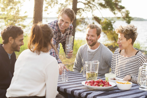 Eine Gruppe von Freunden genießt das Mittagessen am Seeufer, lizenzfreies Stockfoto