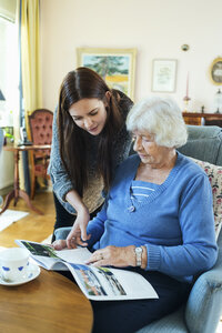 Großmutter und Enkelin lesen gemeinsam eine Zeitschrift im Wohnzimmer - MASF05031
