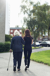 Full length rear view of elderly woman walking with granddaughter on footpath - MASF05033
