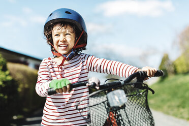 Fröhlicher Junge, der wegschaut, während er mit dem Fahrrad auf dem Fußweg im Hof steht - MASF05041