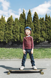 Porträt eines glücklichen Jungen auf einem Skateboard vor einem Baum in voller Länge - MASF05042