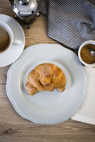 Italienisches Cornetto auf Teller, Buch, Serviette und Kaffeetasse, lizenzfreies Stockfoto