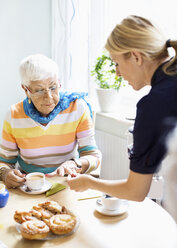 Female caretaker examining senior woman's finger at breakfast table in nursing home - MASF05063