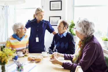 Female caretaker with senior people discussing at breakfast table in nursing home - MASF05064