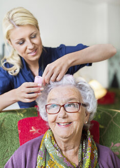 Pflegerin, die einer älteren Frau im Pflegeheim Lockenwickler aufs Haar legt - MASF05065