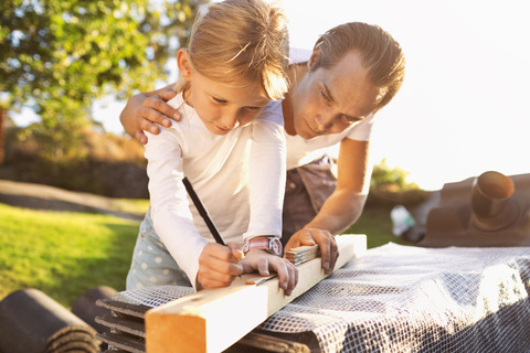 Vater hilft Tochter beim Ausmessen der Planke, lizenzfreies Stockfoto