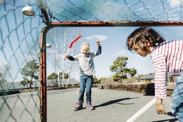 Aufgeregtes Mädchen gestikuliert beim Hockeyspielen mit einem Jungen im Garten - MASF05088