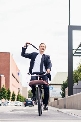 Glücklicher Geschäftsmann in voller Länge, der seine Krawatte abnimmt, während er auf der Straße Fahrrad fährt, lizenzfreies Stockfoto