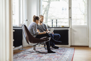 Paar in voller Länge beim Online-Shopping auf Stühlen sitzend zu Hause - MASF05109