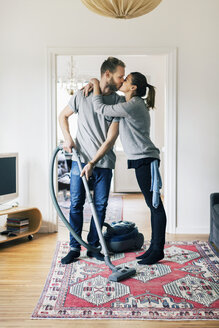 Mann küsst Frau in voller Länge beim Staubsaugen des Teppichs zu Hause - MASF05110