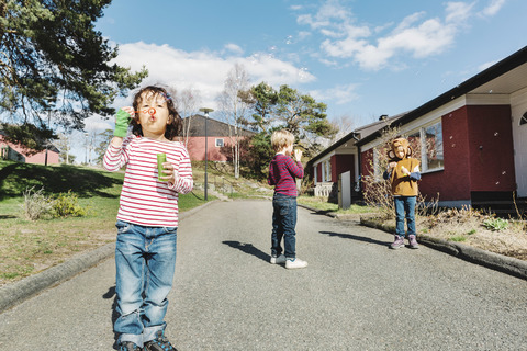 Freunde spielen mit Seifenblasenstäben auf dem Fußweg im Hof, lizenzfreies Stockfoto