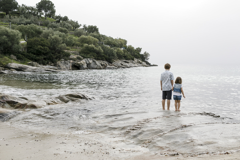 Griechenland, Chalkidiki, Rückenansicht von Bruder und kleiner Schwester am Meer stehend, lizenzfreies Stockfoto