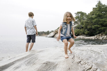 Griechenland, Chalkidiki, Porträt eines glücklichen kleinen Mädchens am Strand mit Bruder im Hintergrund - KMKF00161